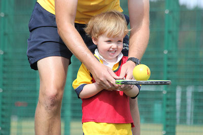 enfant faisant du mini-tennis dans le Val d'Allos avec la monitrice de tennis dans l'exercice où il faut garder la balle  de tennis sur la raquette en marchant